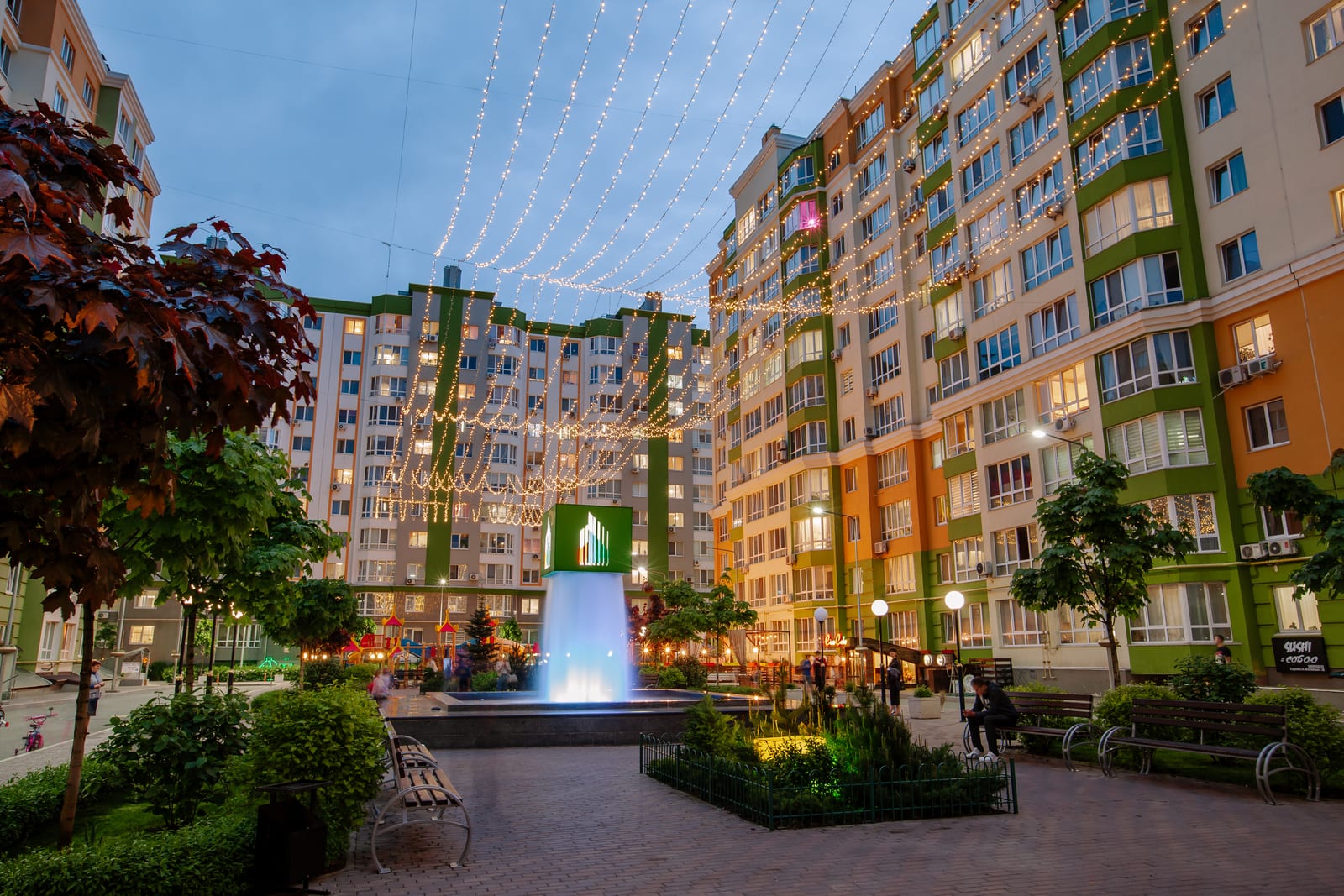 Evromisto by SAVO in the Kyiv region: the courtyard in the evening with a lit fountain, garlands over the walkway and benches