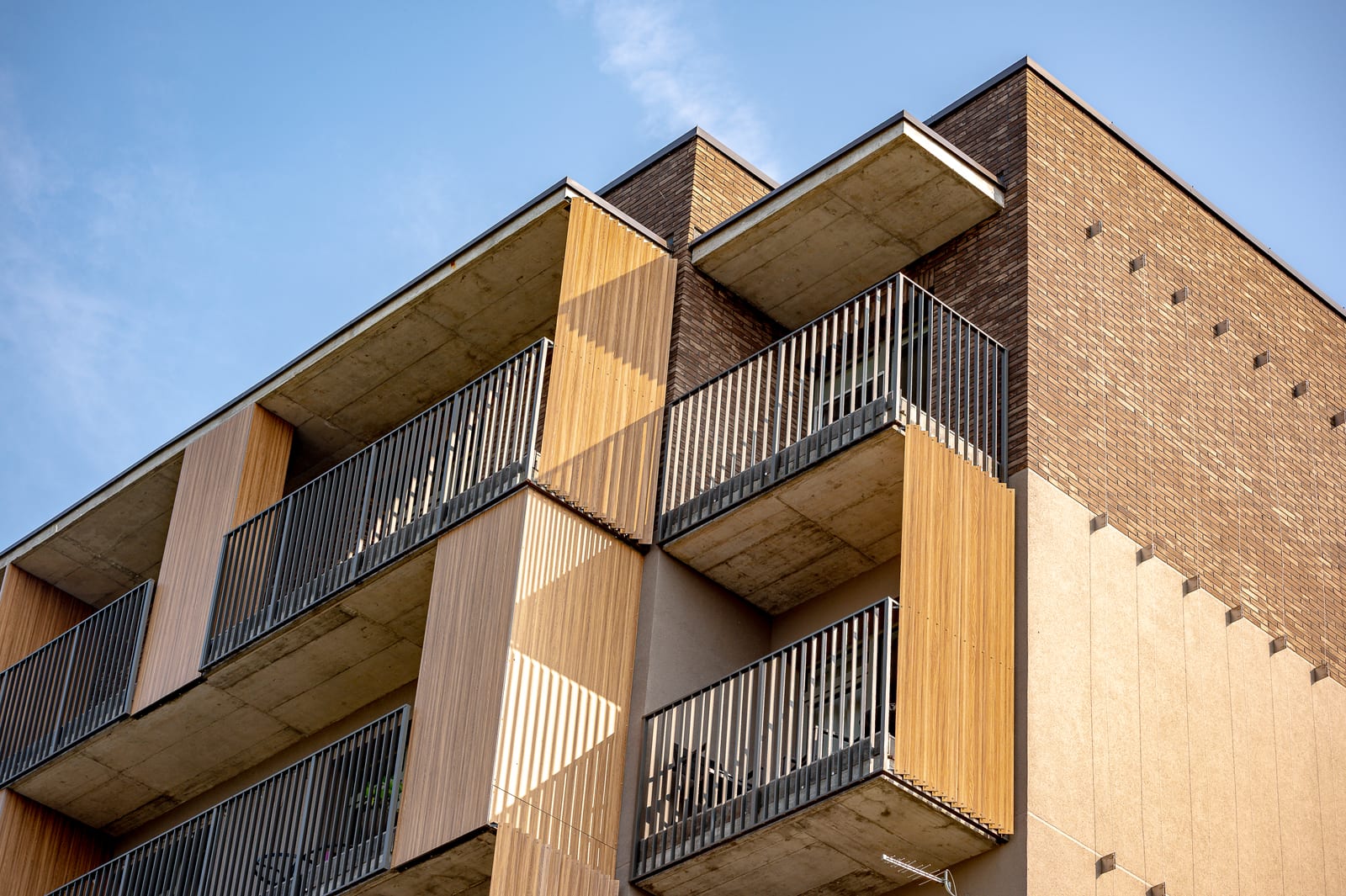 The corner of the Vilnius building by SAVO against a clear sky: cantilevered balconies, timber panels and clinker brickwork