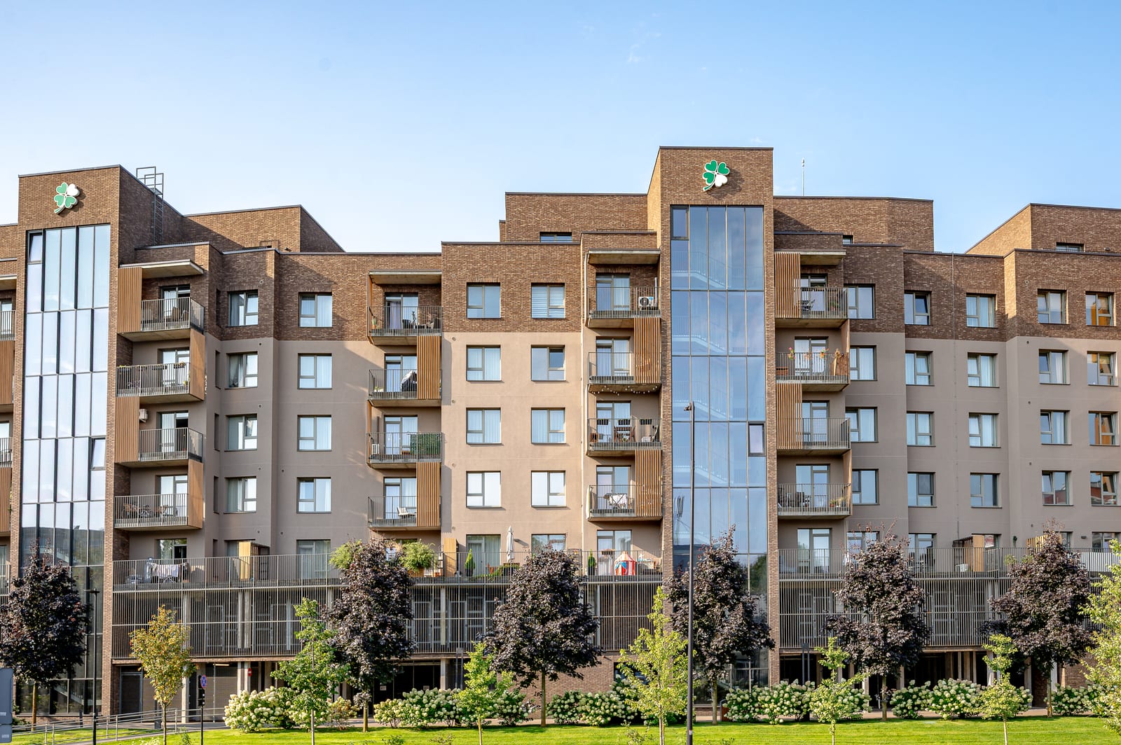 Lucky Homes by SAVO in Vilnius: the full row of clinker-brick blocks with a glazed stair tower, seen from the lawn