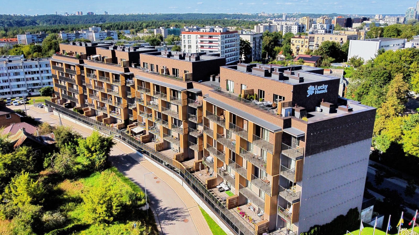 Lucky Homes by SAVO in Vilnius from the air: the lit name on the end wall, planted roof terraces and the city of Vilnius on the horizon