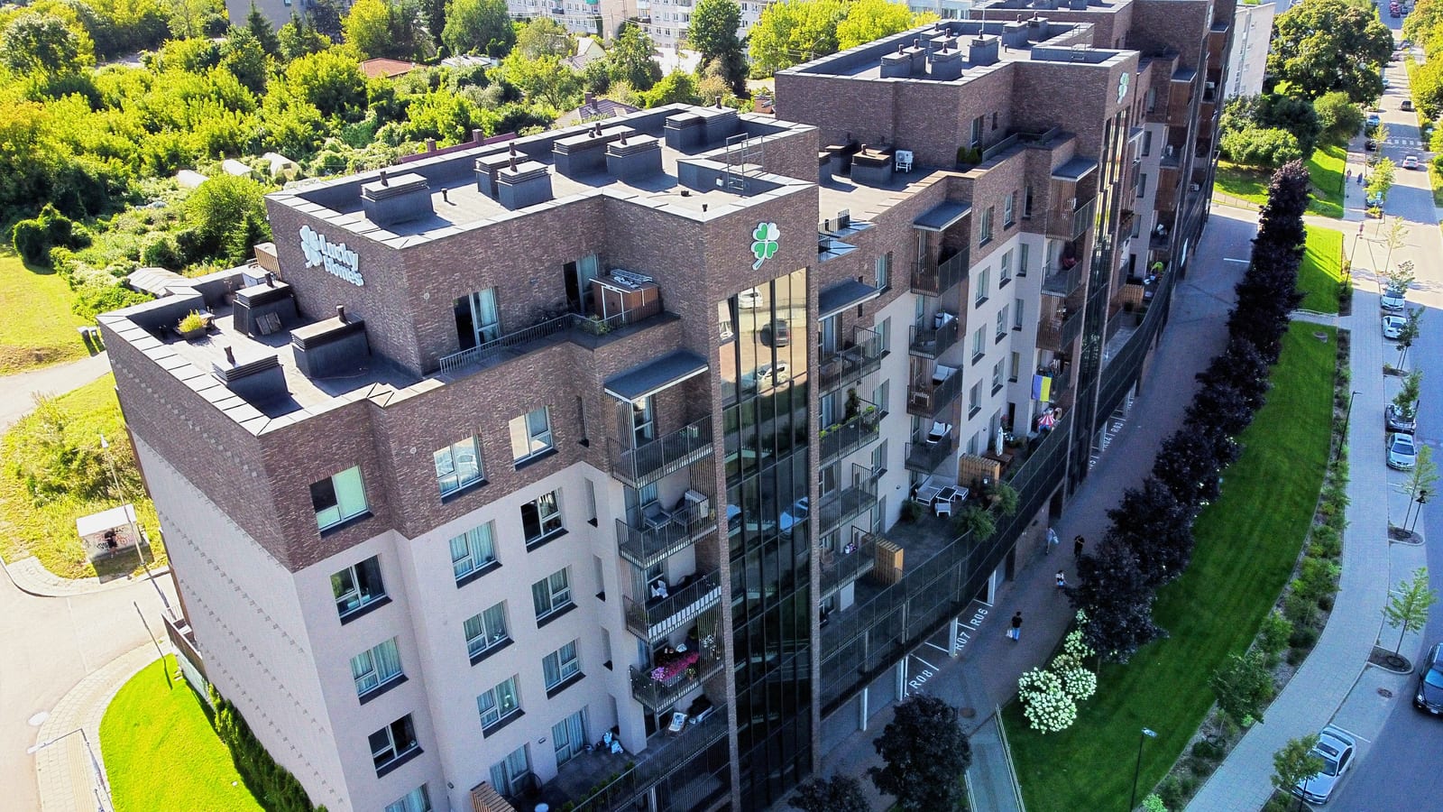 The L-shaped block from above: flat roofs, the inner side of the courtyard, lawns and clipped hedges, and the access road running along the building.